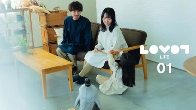 A man, woman, and child part of a family sit in a living room while interacting with LOVOT, which is standing on the floor looking at them.