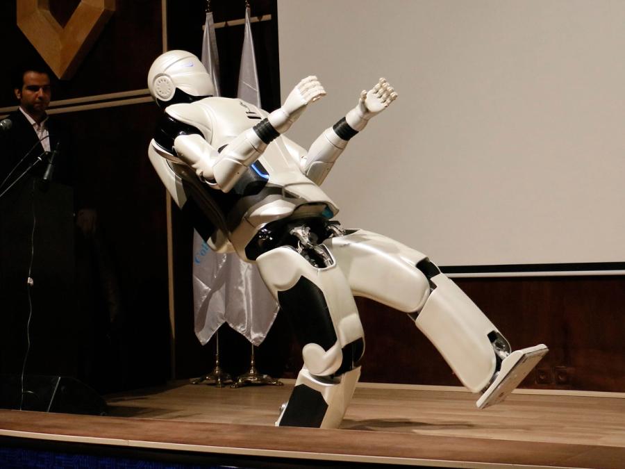 An adult-size humanoid robot leans backwards while standing on its right foot.