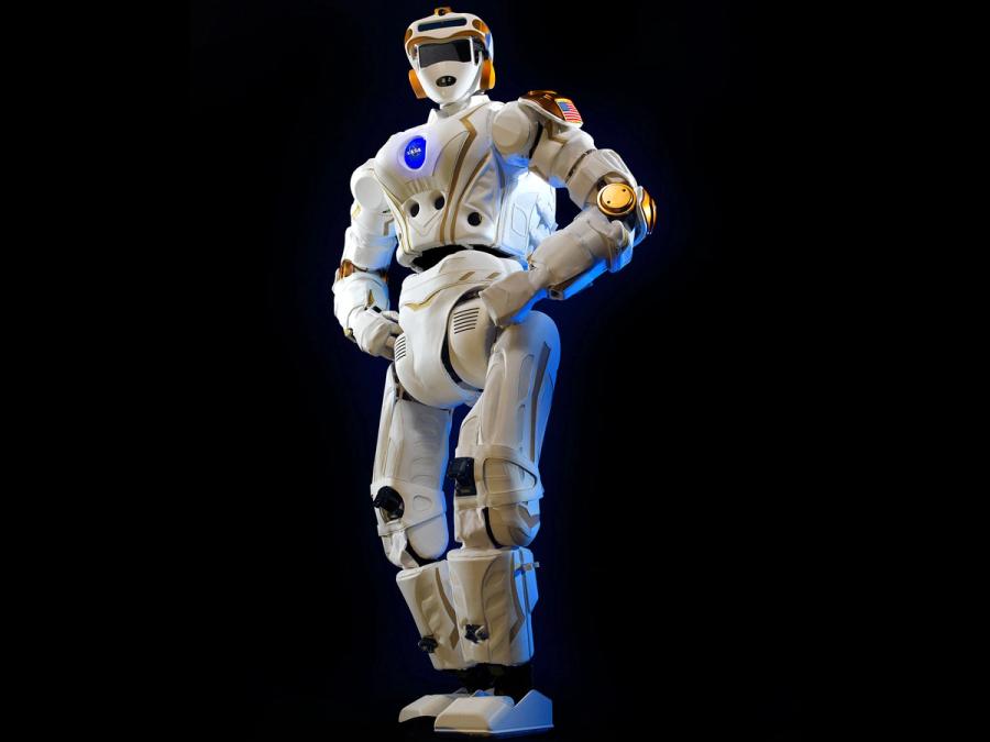 A high-tech humanoid stands in a power pose with hands on its hips. It's appearance resembles an astronaut, with its white jointed body, helmet with gold accents, and chest plate with the NASA logo.