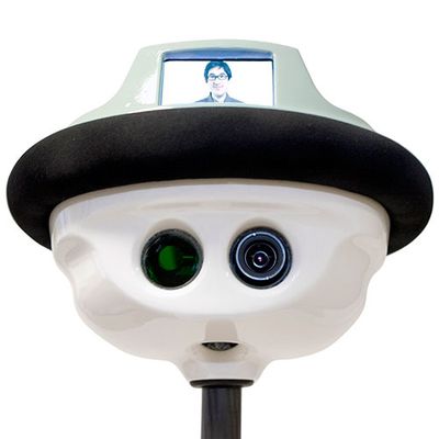 Close up of QB's shiny white head with has two camera eyes, mouth, and the appearance of a hat, which has a screen showing a mans smiling face.