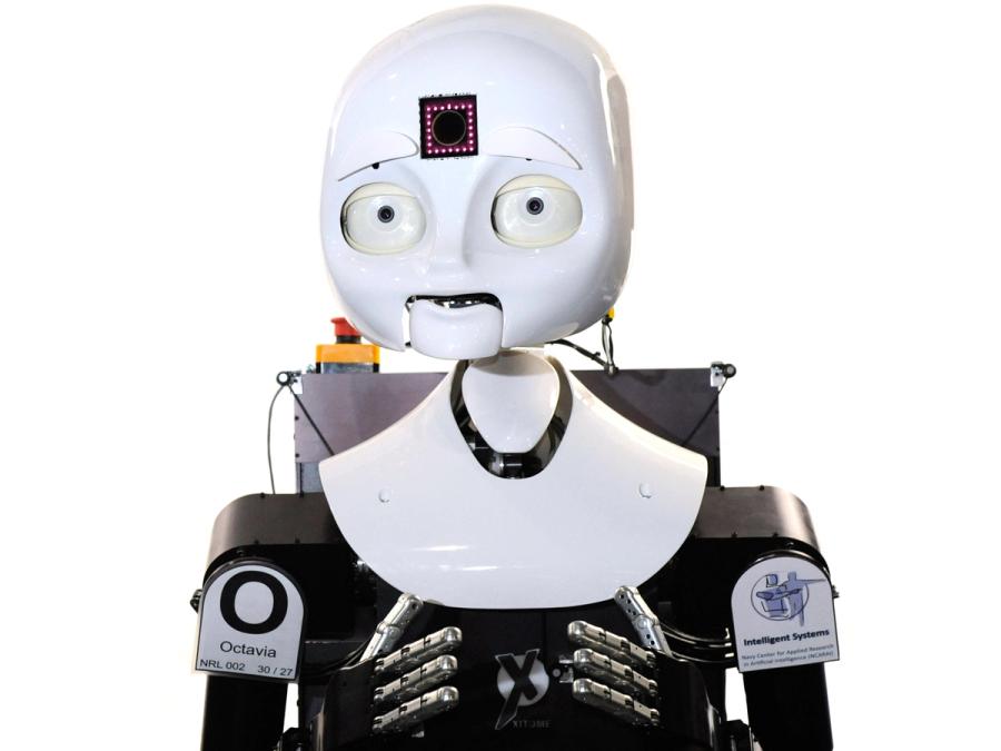 The robot has an expressive white face with eyes, nose, mouth, and a glowing square in its forehead. The robot has two arms with jointed human like silver fingers.