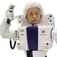 A male humanoid robot with fluffy white hair and a mustache in the style of Albert Einstein waves.