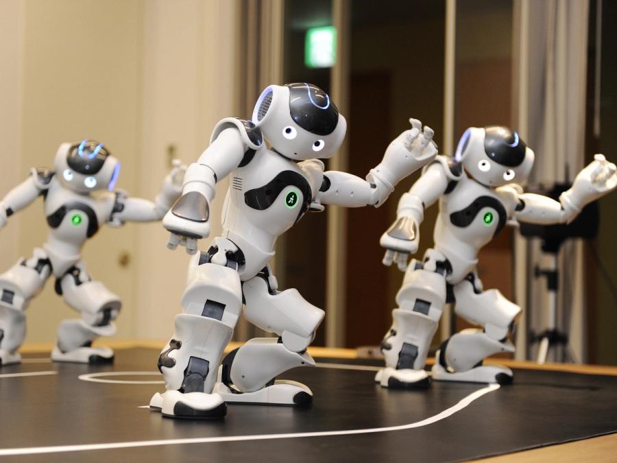 Three white and silver Nao humanoid robots doing coordinated dance moves.