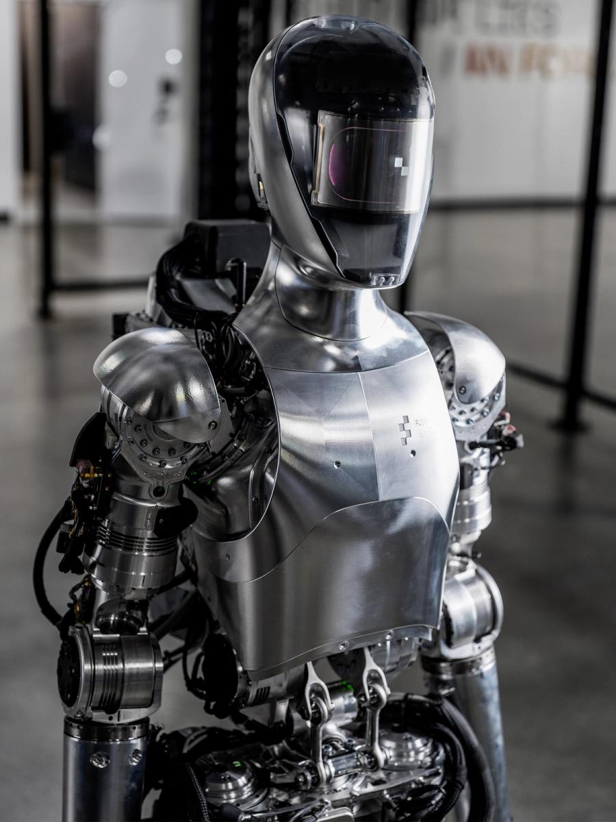 A waist up view of Figure 01, a shiny silver humanoid robot with a helmeted head.