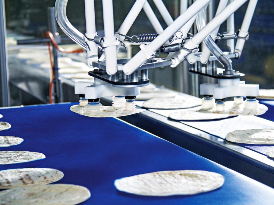 Closeup of grippers on a pick and place machine. Tortillas line the surface, and two are seen being held by grippers.