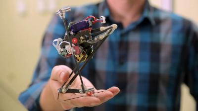 A small one-legged robot stands on a man's palm.