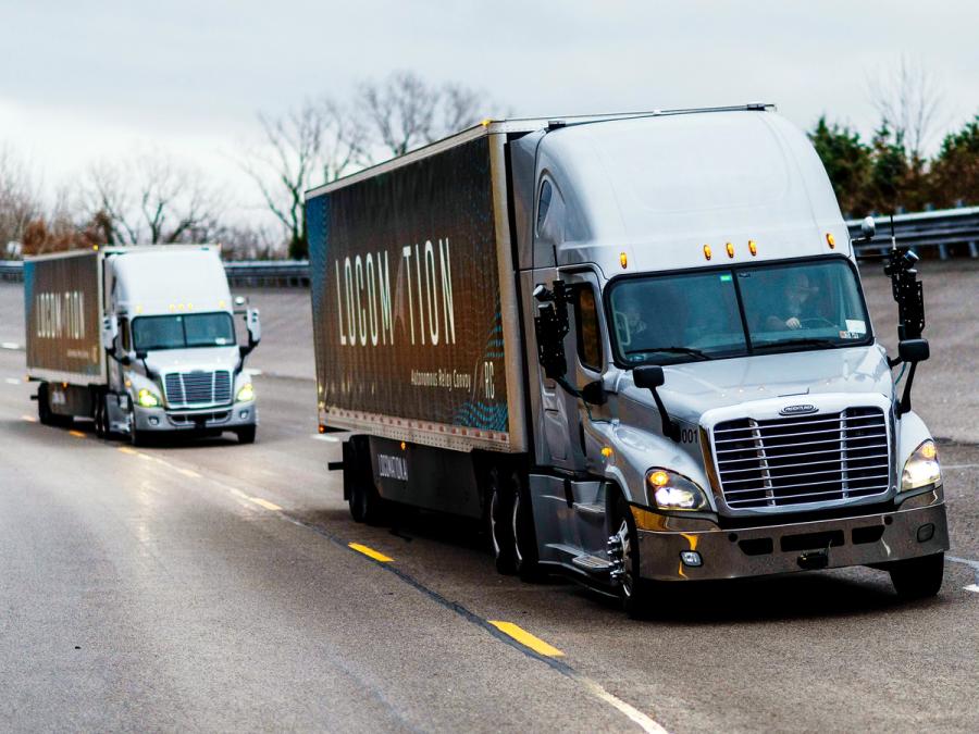 Two silver freight trucks that says Locomation on the side, in a row, driving on a highway.