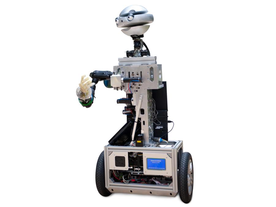 An expressive robot with a silver robotic head segmented head has a torso with electronics, and a wheeled base.