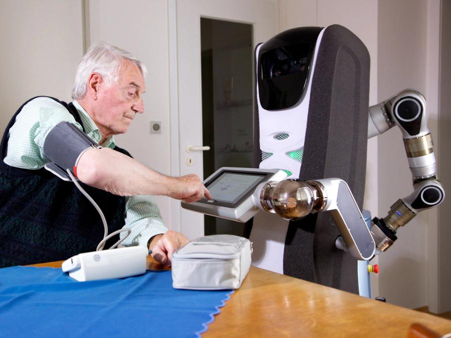 A robot holds a display up to an elderly man taking his blood pressure.