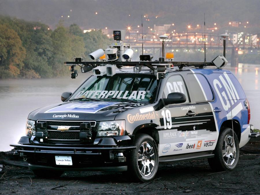 An SUV mounted with cameras and tech on top, and covered in logos.