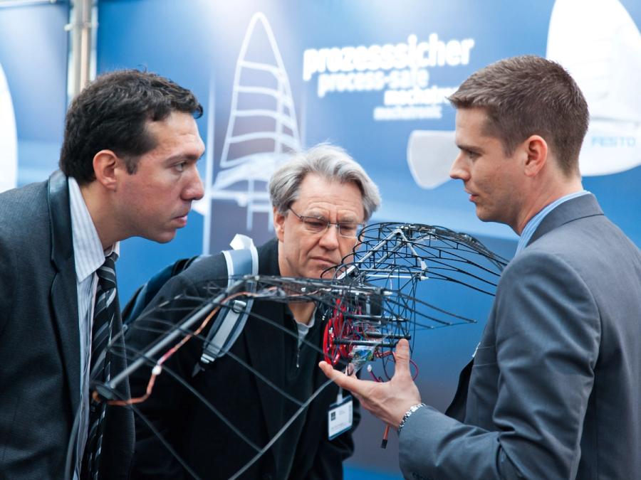 Three men observe the robotic skeleton at a trade show.