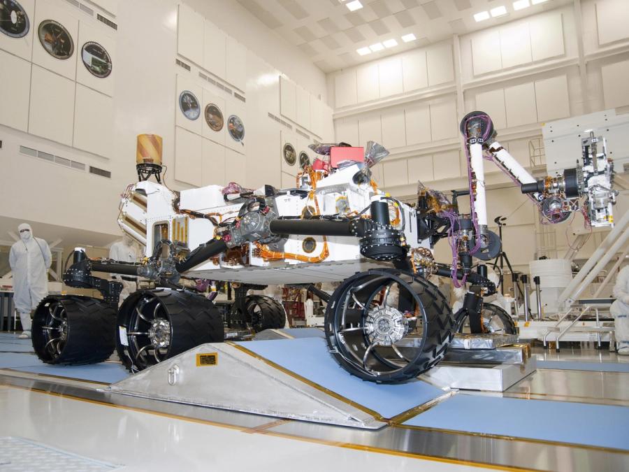 A six-wheeled robotic vehicle's wheels move it over a triangular ramp.