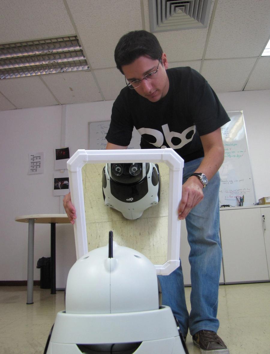 The robot sees its reflection in a mirror that a man is holding up to it.