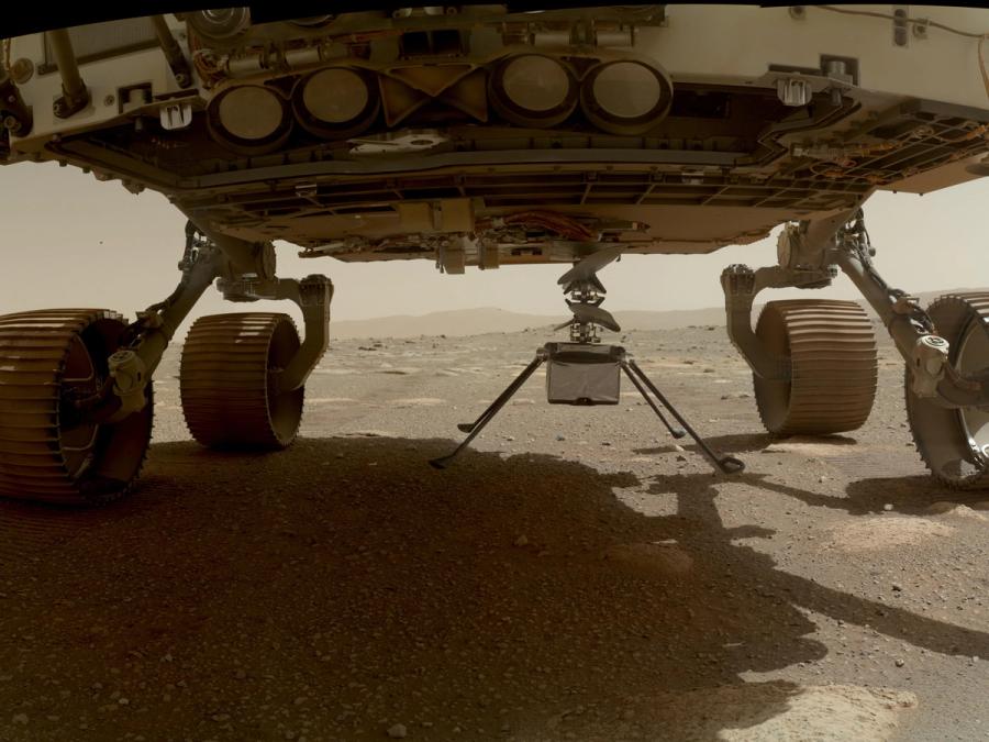 The helicopter's four spindly legs touch done on Martian soil as it deploys from underneath a much larger rover.