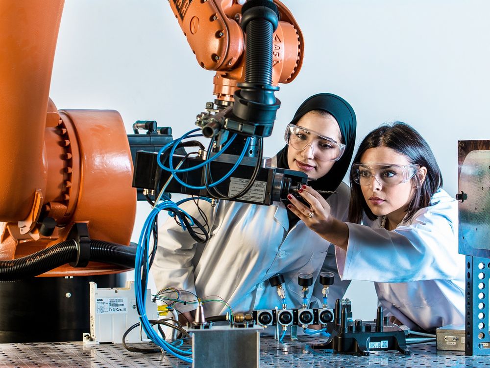 A photo of two women looking at a robotic arm.  