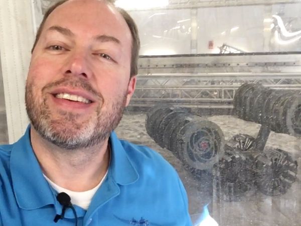 Male robotics engineer looks at camera with robot in the background.