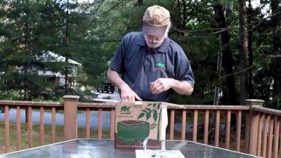 Man wearing a hat unboxes a robot outside.