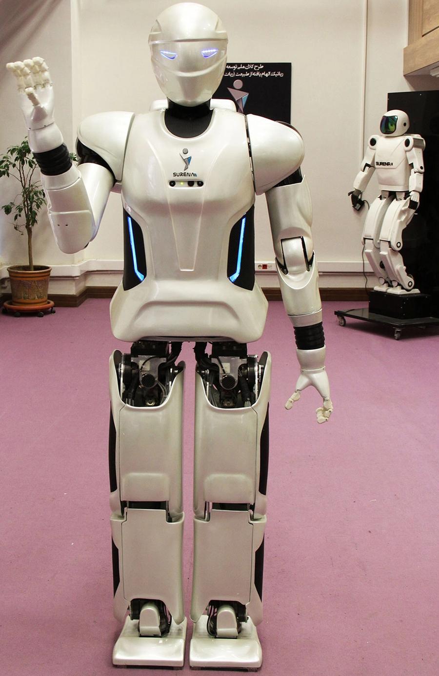 An adult-size humanoid robot waves its left hand.