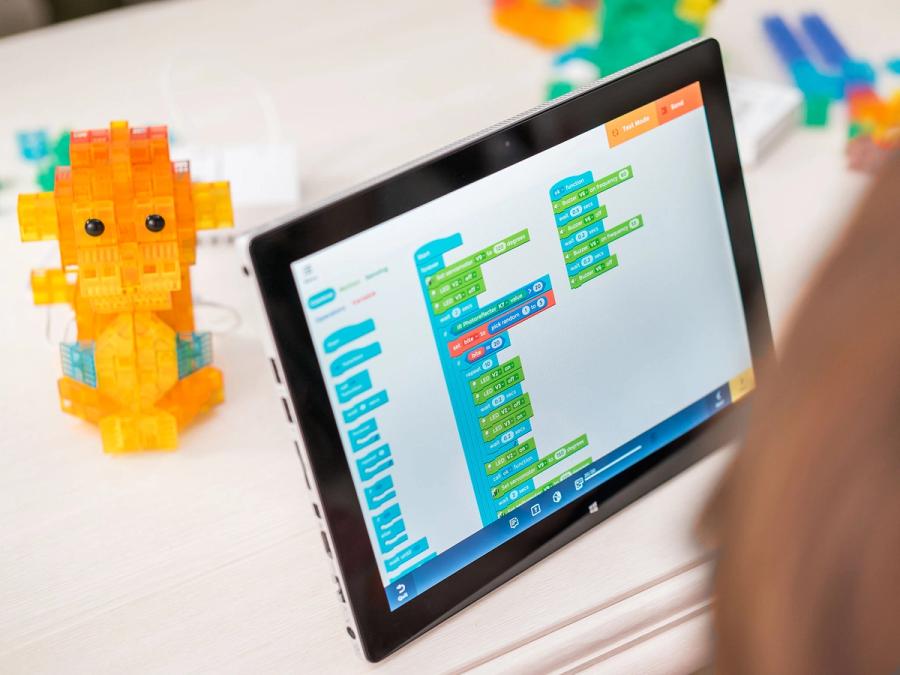 A tablet screen shows simple programming of a monkey shape built on the table.