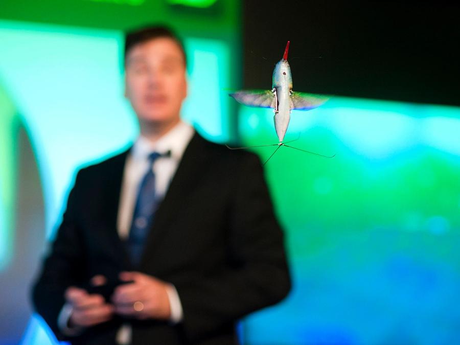 The robot flies in the air in front of a man who is blurry in the background.