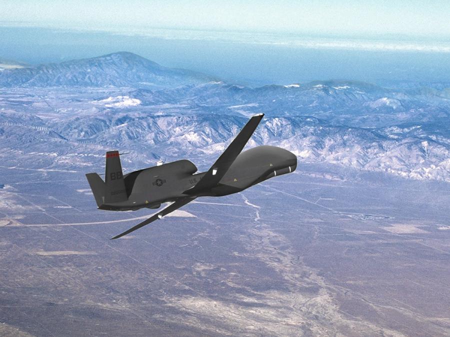 A view of the Global Hawk UAV as it flies over a barren landscape.