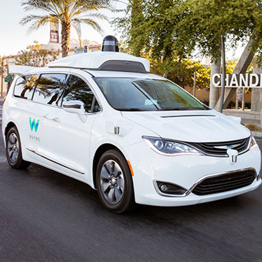 A white car labelled Waymo has an extra white piece on its roof, which is topped with a black object.