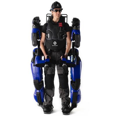 A person wearing all black, including safety glasses and a hard hat, is wearing a full body blue and black exoskelton.