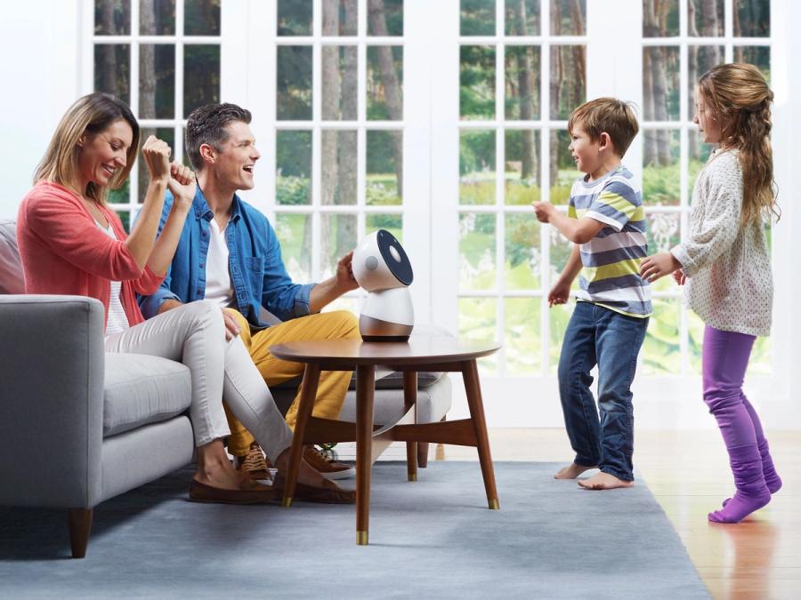 A mom, dad and a small white tabletop robot called Jibo look at two dancing children.