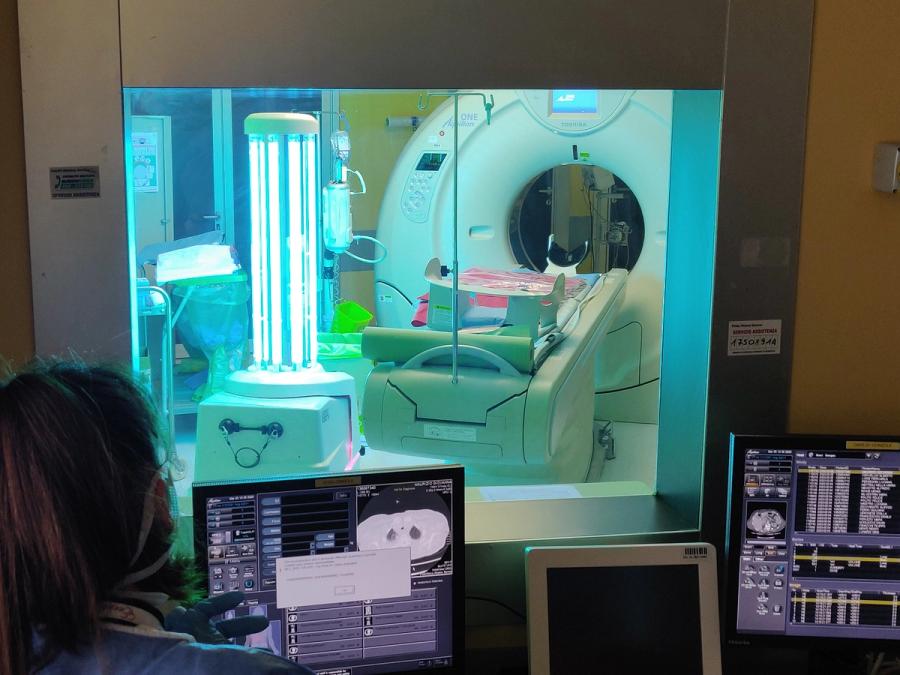 A radiologist works at a computer in front of a window into a room with an MRI machine and a mobile UVD disinfecting robot.