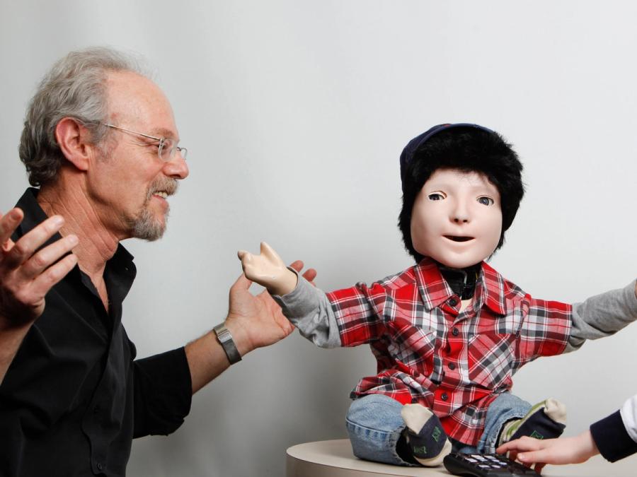 A man with grey hair and glasses adjusts the robot.