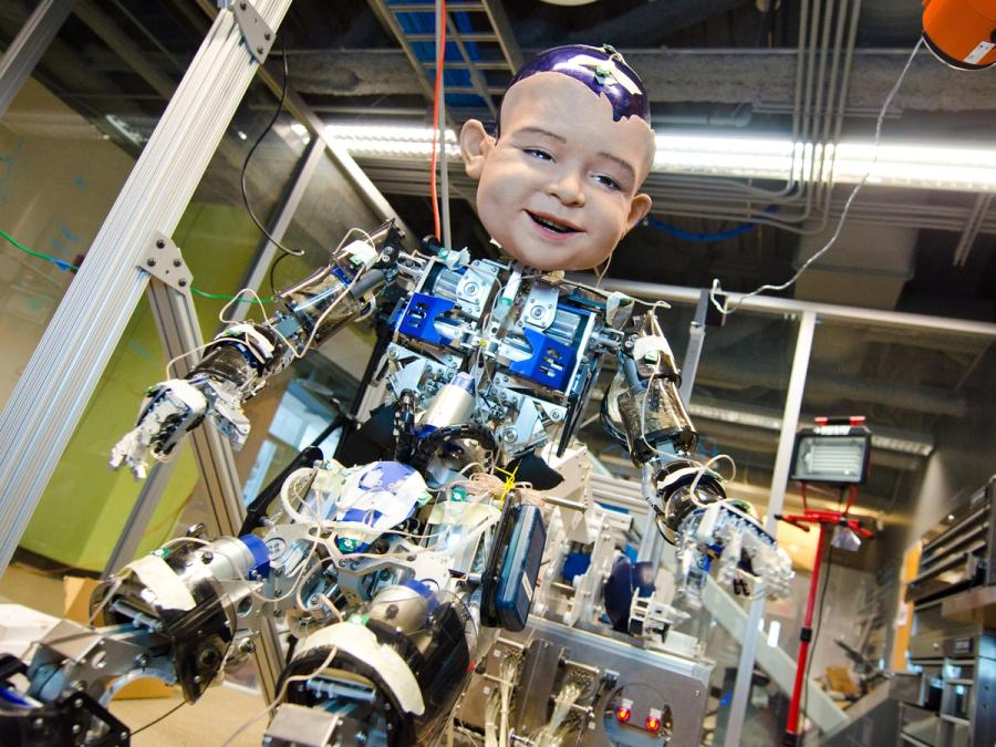 A child sized humanoid robot with exposed electronics in the torso, arms and legs, and an overly large expressive child's face.